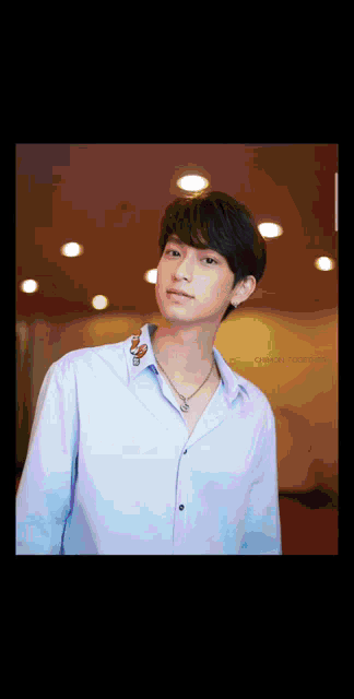 a young man wearing a blue shirt and a necklace is standing in a room