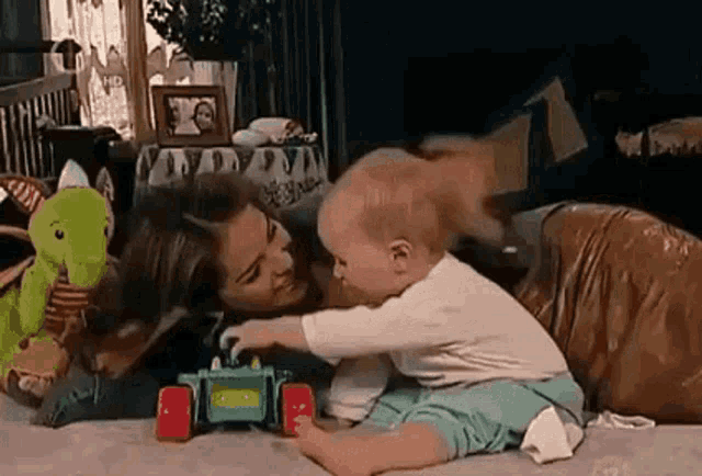 a woman is laying on the floor with a baby playing with a toy truck .