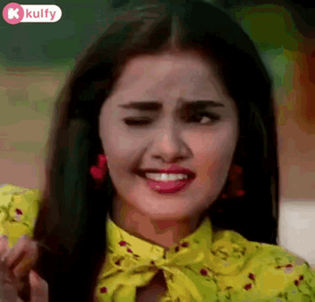 a woman wearing a yellow shirt and red earrings is making a funny face