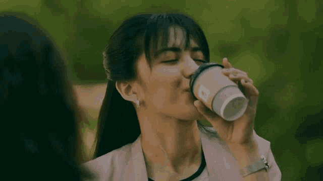 a woman is drinking a cup of coffee from a disposable cup