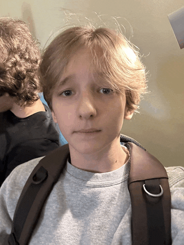 a young boy wearing a grey shirt and a brown backpack