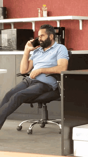 a man with a beard sits in an office chair drinking from a cup