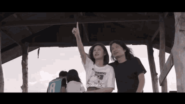a man and a woman are standing under a wooden structure and the woman is wearing a shirt that says " torment " on it