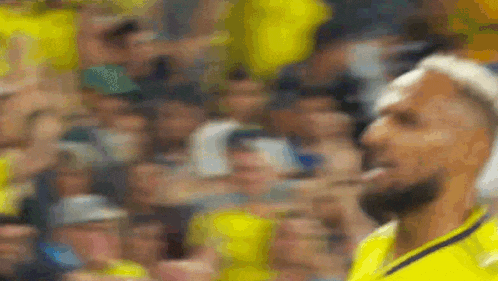a blurry picture of a man in a yellow shirt standing in front of a crowd of people .