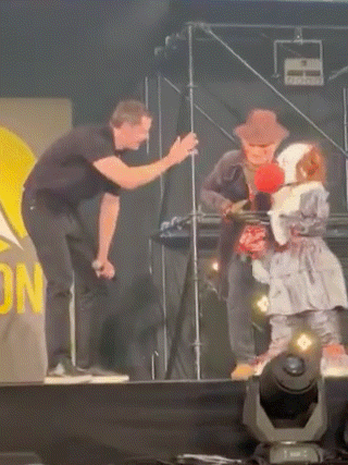 a man in a black shirt is standing on a stage next to a man in a cowboy hat .