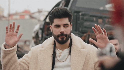a man with a beard wearing a white coat and a gold chain