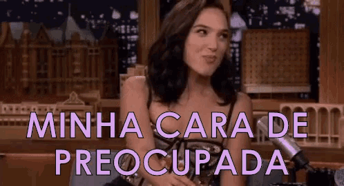 a woman is sitting in front of a microphone with the words minha cara de preocupada written on the screen .