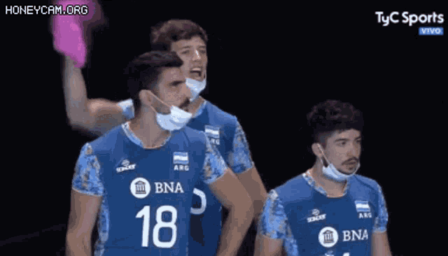 a group of volleyball players wearing face masks are standing next to each other on a field .
