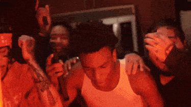 a group of people are gathered around a man in a white tank top