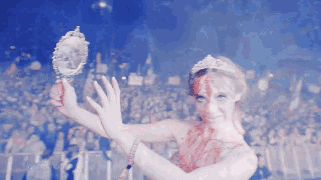 a woman with blood on her face holds a mirror in front of a crowd