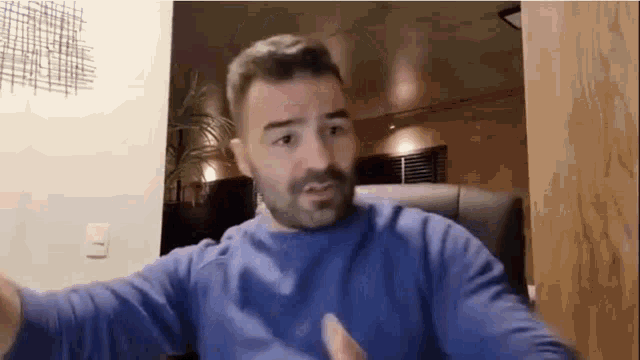 a man with a beard is wearing a blue sweater while sitting in a chair .