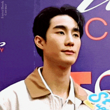 a young man wearing a white shirt and a brown jacket is standing in front of a sign .