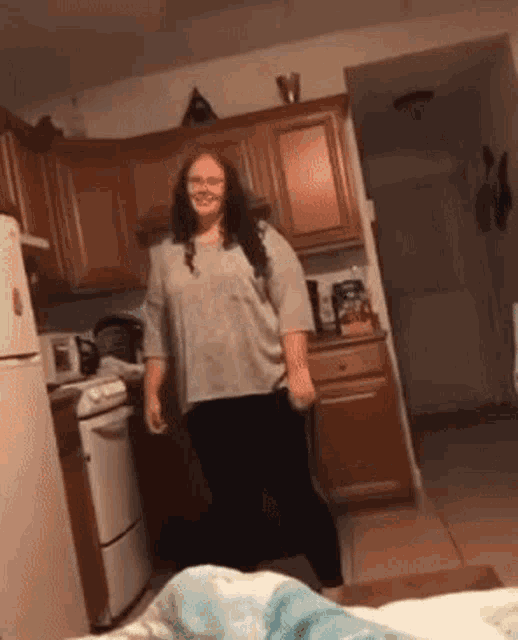 a woman is standing in a kitchen wearing glasses and smiling