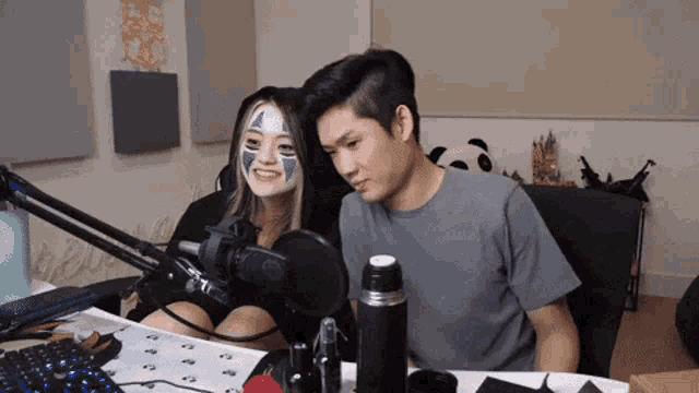 a man and a woman are sitting in front of a microphone with a panda in the background
