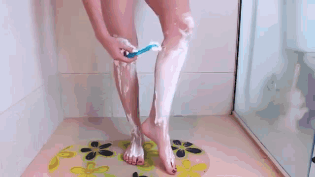 a woman is shaving her legs in a bathroom with a toothbrush