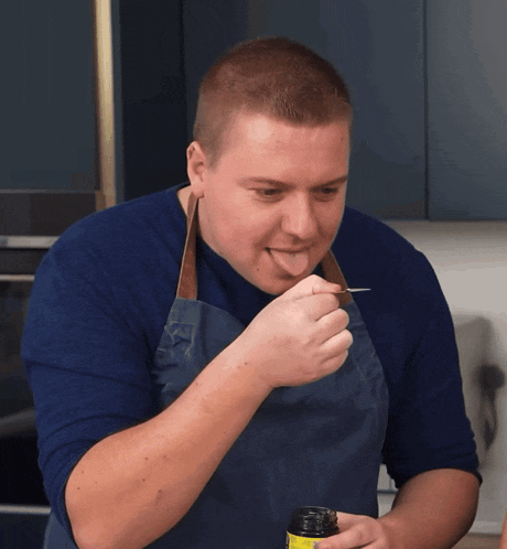 a man wearing an apron is licking a spoon from a jar