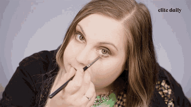a woman is applying eye shadow with the elite daily logo behind her