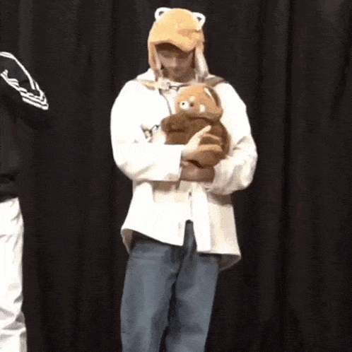 a man is holding a teddy bear in his arms while wearing a hat .