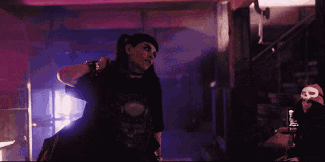 a woman in a black shirt with a skull on it is standing in a dark room