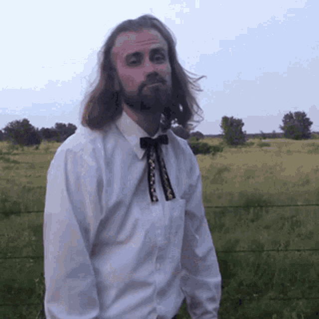 a man with long hair and a beard is wearing a white shirt and bow tie