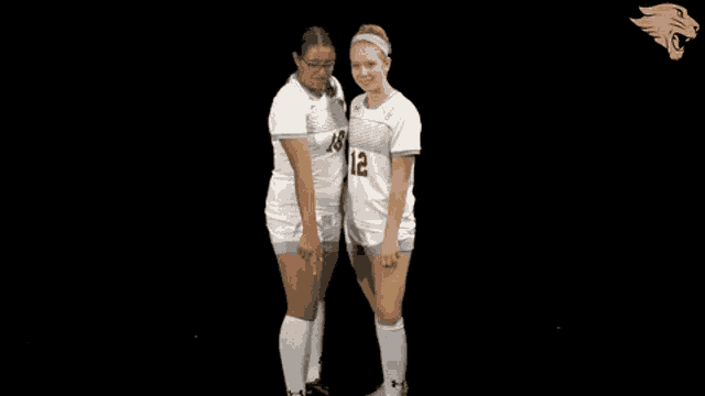 two female soccer players standing next to each other one with the number 12 on her jersey