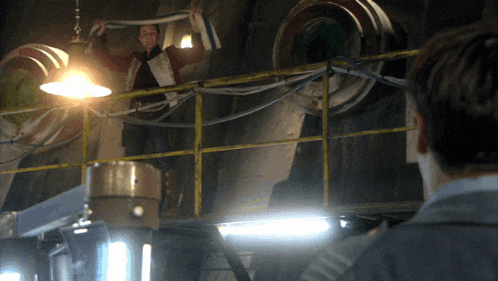a man is standing on a railing holding a hose while another man looks on