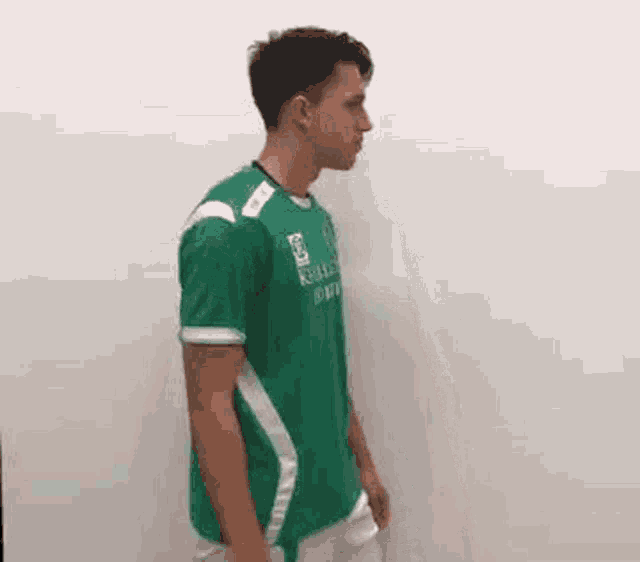 a young man is wearing a green t-shirt and white shorts .