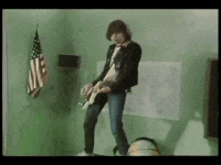 a man is playing a guitar in a room with an american flag hanging on a wall .