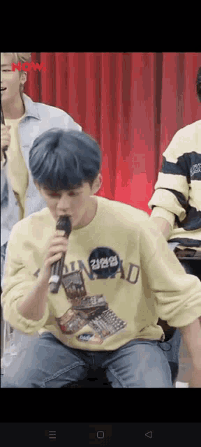 a man with blue hair is singing into a microphone while wearing a yellow shirt .