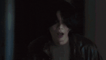 a man with curly hair is standing in front of a window in a dark room .