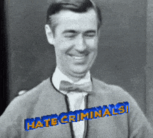 a man wearing a bow tie and a sweater that says hate criminals is smiling