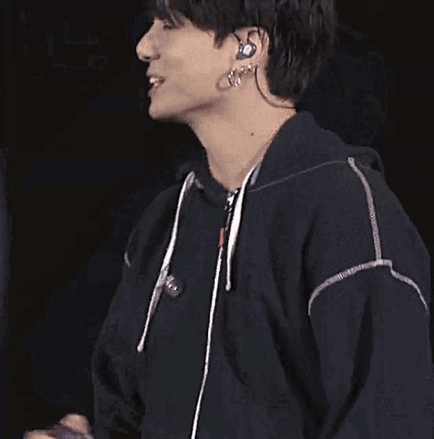 a young man in a black hoodie is holding a microphone and wearing earrings .