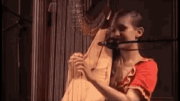 a woman is playing a harp with a microphone in front of her .