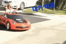 a little boy is driving a red toy car on the street .