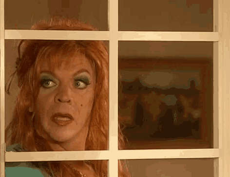 a woman with red hair and blue eye shadow looks out a window