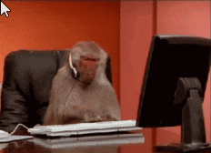 a monkey wearing headphones sits at a desk in front of a computer monitor