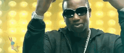a man wearing sunglasses and a watch is standing in front of a yellow background with his arms in the air .