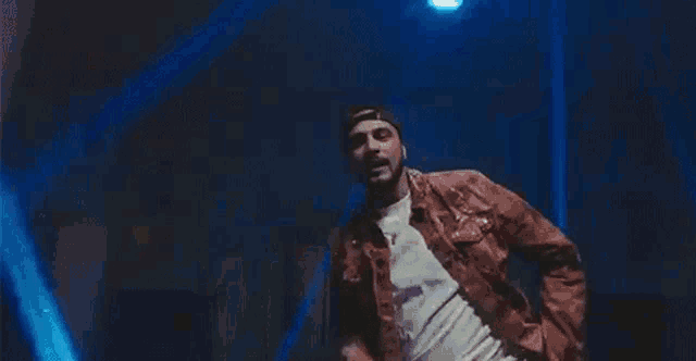 a man in a red jacket and hat is dancing in front of a blue light .