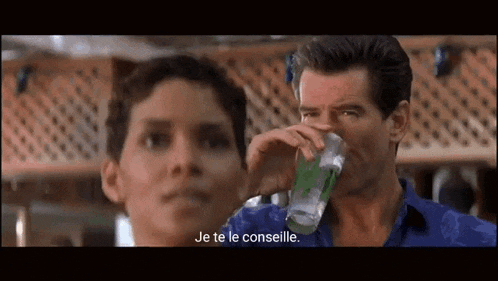 a man is drinking a glass of water while a woman watches .