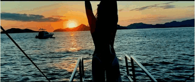 a woman in a bikini stands on a boat watching the sunset