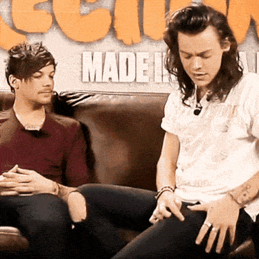 two men are sitting on a couch in front of a wall that says made in orange letters