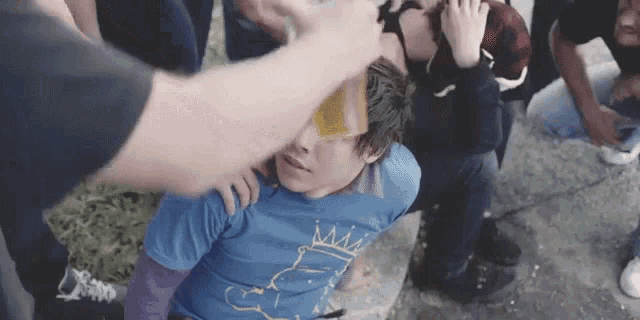 a boy wearing a blue shirt with bart simpson on it is being slapped by a group of men .