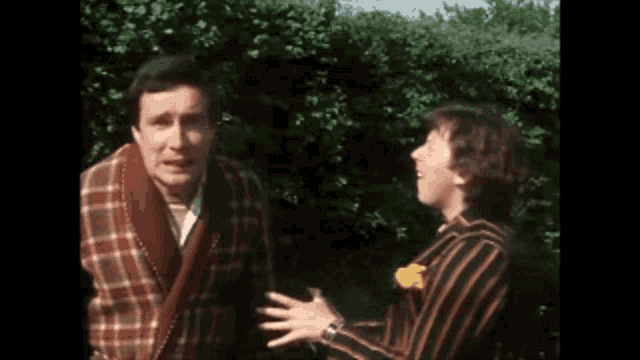 two men are standing next to each other in front of a hedge