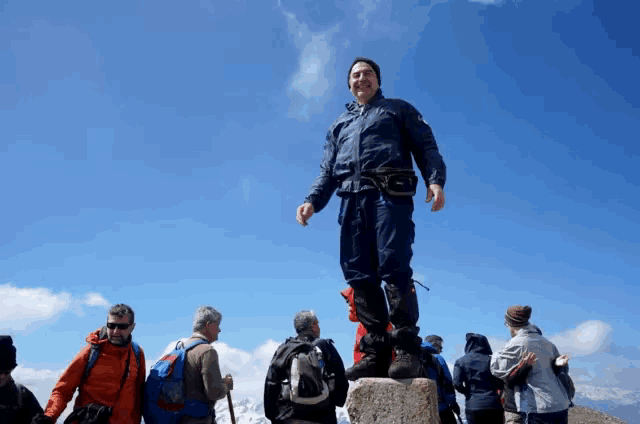 a man stands on top of a stone pillar surrounded by other people