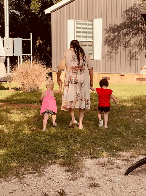 a woman in a floral dress walks with two little girls