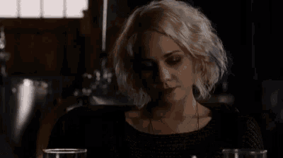 a woman with blonde hair is sitting at a table with two glasses of wine .