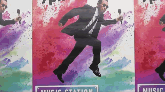 a man in a suit and tie is jumping in the air while holding a microphone in front of a sign that says music station