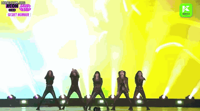 a group of women are dancing on a stage with a green background and a kcon logo in the background