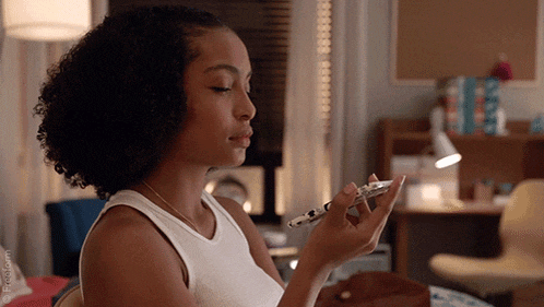 a woman in a white tank top holds a cell phone in her hand