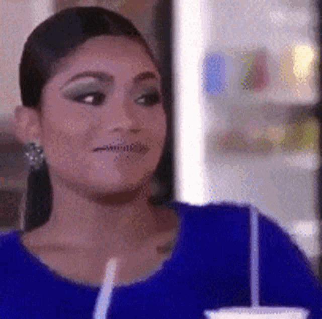 a woman in a blue shirt is drinking from a cup with a straw